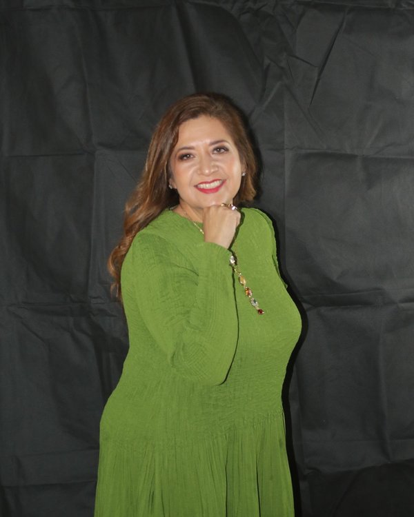 Cris standing in a green dress against a dark studio background